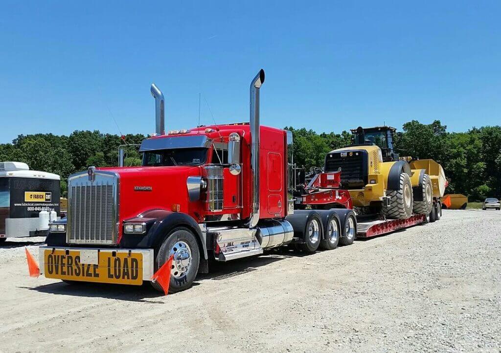 Red Kenworth truck hauling a Caterpillar wheel loader on a lowboy trailer