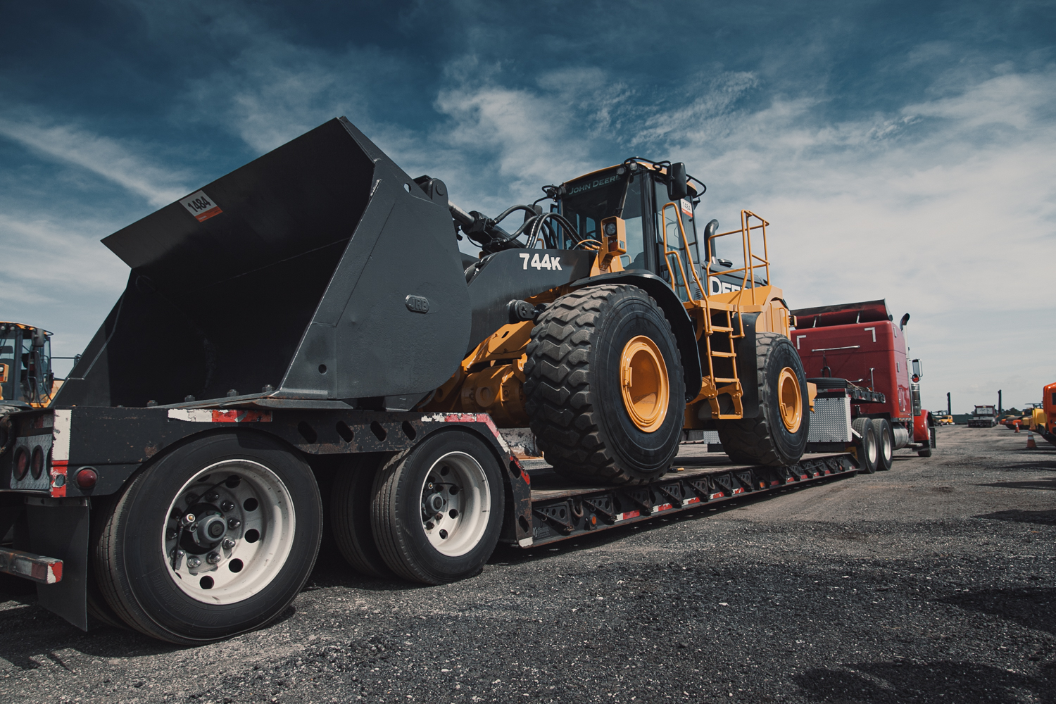 John Deere wheel loader secured on a lowboy trailer behind a red semi-truck